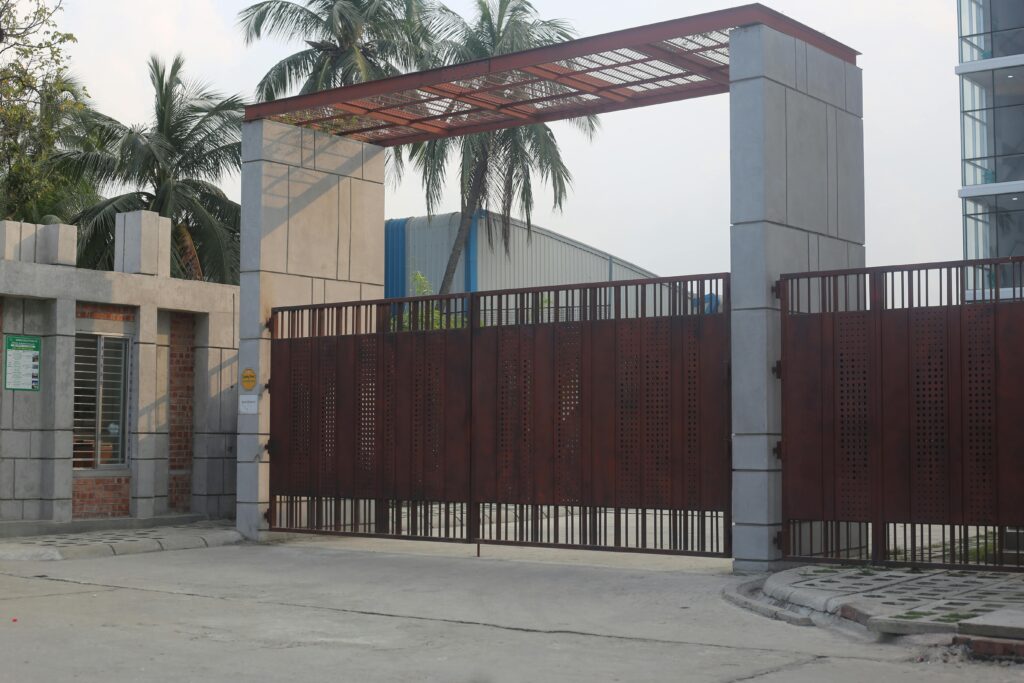 A large automated iron gate as the entrance to a modern urban building, surrounded by palm trees.